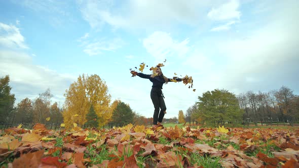A Young Girl Schoolgirl Whirls with Autumn Leaves in the City Park alt