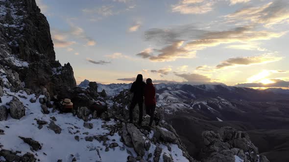 Aerial View of a Young Couple Standing on a Cliff High in the Mountains at Sunset