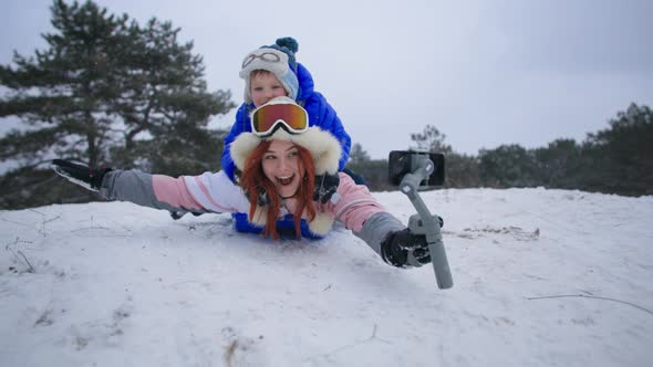 Fun Winter Holidays Joyful Woman with Her Son Slides Down a Snowy Hill on a Sled with a Mobile Phone