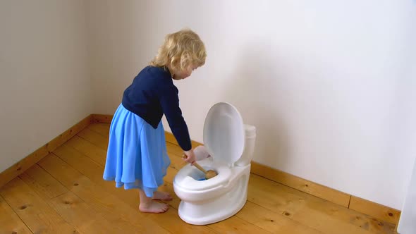 A child cleaning a potty toilet with detergent and a brush alt