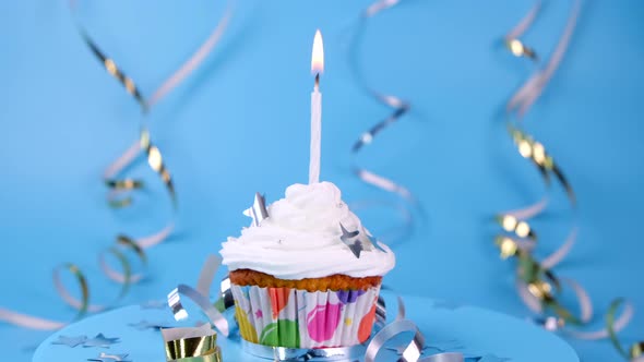 Rotating Birthday Cake for a Boy or Man or a Cupcake with a Burning Candle on a Blue Background
