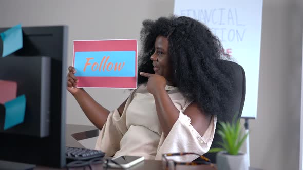 Successful Cheerful African American Blogger Showing Follow Sign Smiling Looking at Monitor alt