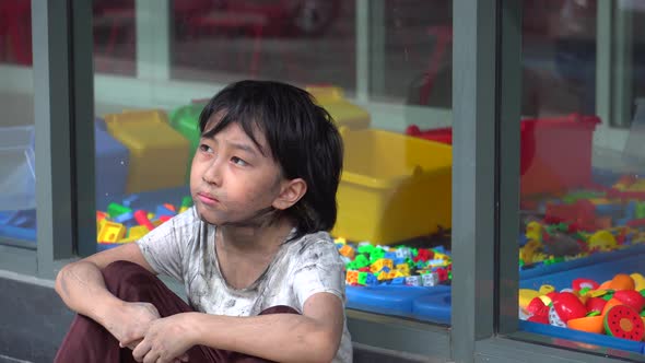 Young Southeast Asian dirty homeless boy looking into window wherein colorful toys lie, longing for alt
