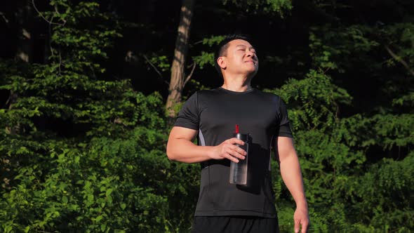 Athletic Korean Man Holding Bottle of Water Takes a Deep Breath After Training alt
