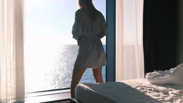 A Peaceful Happy Young Blonde in a Bathrobe Enjoys Her Morning Coffee Standing Against the Backdrop