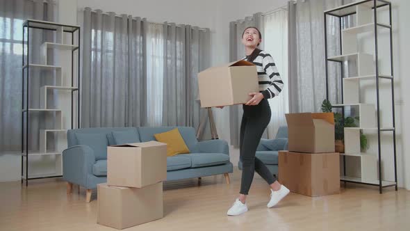 Young Asian Woman Carrying Cardboard Box With Stuff Into A New House And Looking Around alt