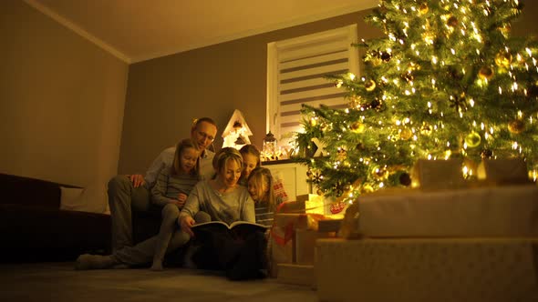 Parents With Children at Christmas Tree Reading a Book