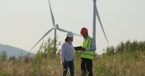 Customer and Engineer Looking at Tablet To Order. Windmills in the Background alt