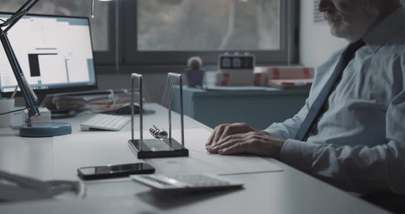 Corporate businessman sitting at desk and playing with Newton's cradle balance balls