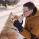 Young man with Akita Inu dog in park. Snowy winter background. Sunny day. - VideoHive Item for Sale