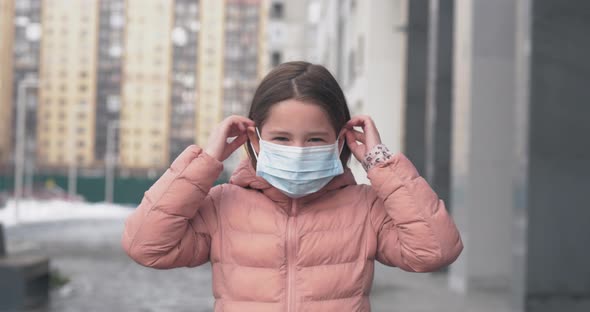 Coronavirus Protection. A Caucasian Girl Puts on a Medical Protective Mask Standing on a Street