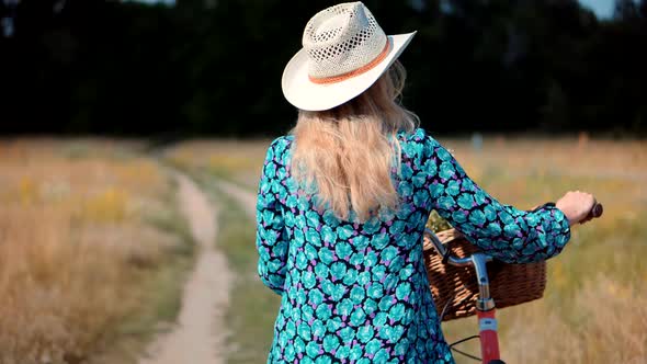 Girl Relaxing On Countryside Wildflower Field.Girl In Hat Enjoying Weekend.Cyclist Walking With Bike alt