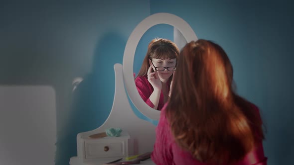 Woman Sitting in Front of a Mirror at Home Puts on Glasses and Smiles
