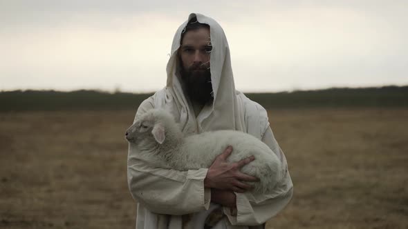 Jesus Christ Holding A Lamb Looking At Camera With Sunset Behind Him