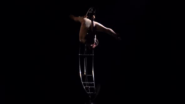 Gymnast in a Brilliant Costume Performs Tricks on a Special Design Moon . Black Background alt