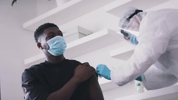 Doctor Wearing a Face Shield Gloves and Mask Giving an Injection to a Guy alt