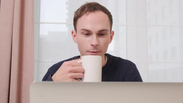 A Man Drinks Coffee and Communicates Via Video Link Using a Laptop