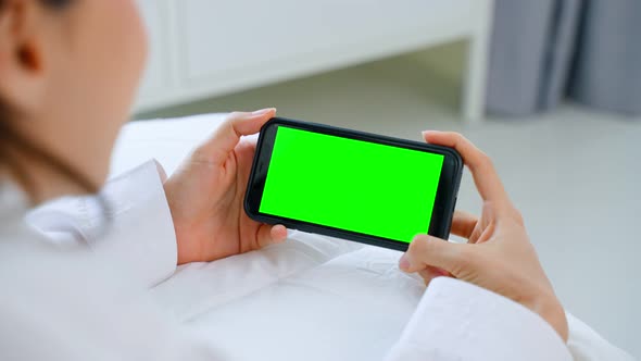 Asian woman talk on online video call after wake up in morning with green screen on bed at home. alt