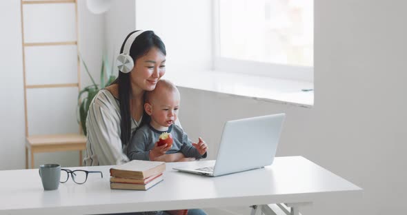 Young Mother Freelancer with Her Child Working at Home Office Using Laptop alt
