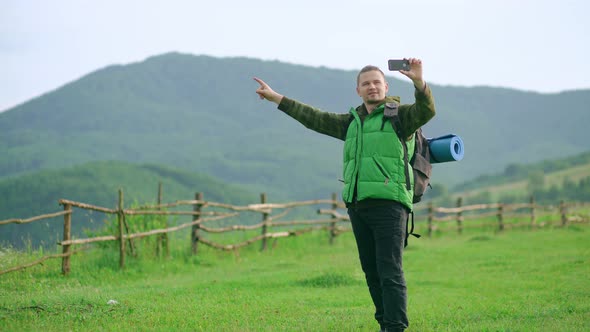 A Tourist with a Backpack Takes a Selfie Against the Backdrop of a Mountain alt