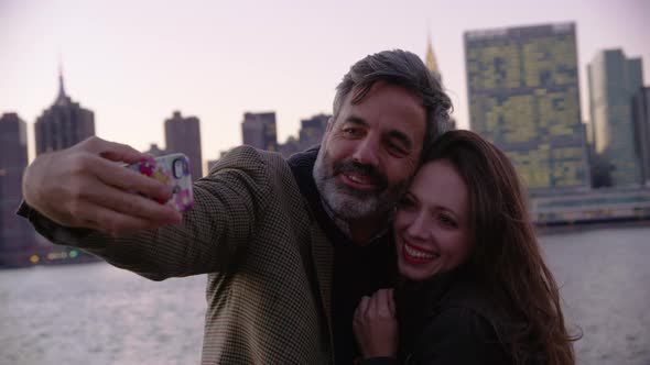 Couple in New York City taking cell phone selfie with city skyline in background