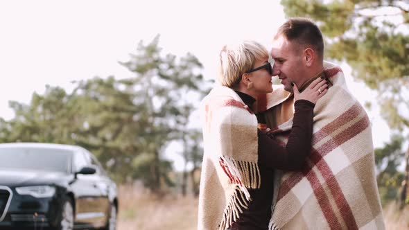 Portrait of Couple Covered with Blanket Embracing in Forest alt