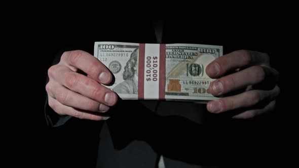 Businessman in Suit Shows Stack of 10000 American Dollars on Black Background alt