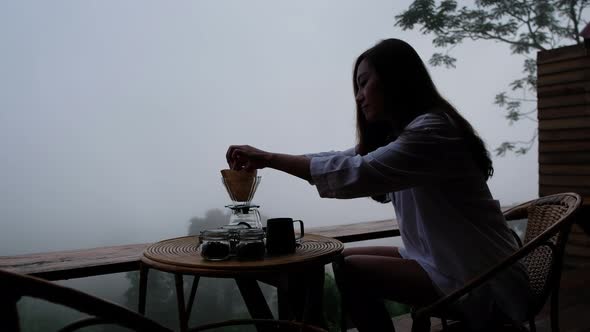 A woman preparing to make drip coffee with a beautiful nature view on foggy day