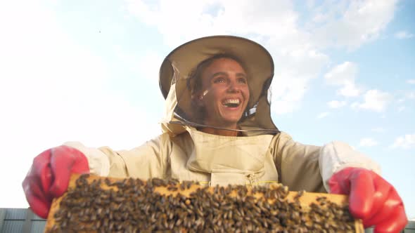 A Girl Beekeeper in a Protective Suit Carries a Frame with Honey From a Bee Hive