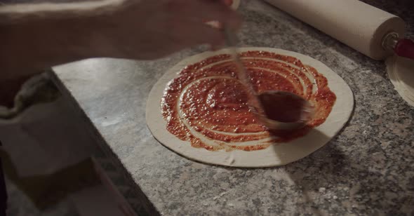 Crop chef smearing tomato sauce on pizza alt