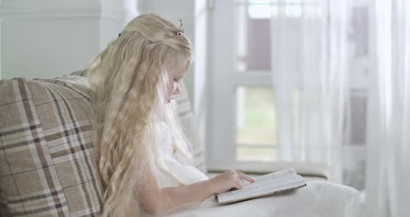 Side View of Blond Caucasian Little Girl Sitting on Sofa and Reading, Santa Coming To Glass Entrance alt