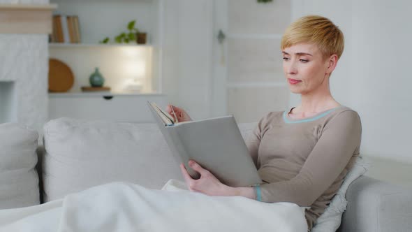 Happy Relaxed Millennial Woman Lying on Comfy Sofa with Paper Book in Hands in Living Room Involved alt