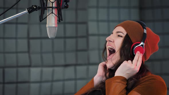 Young woman in headphones emotionally singing in microphone in the sound recording studio alt
