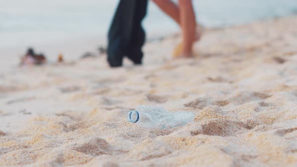 Closeup of Volunteer Picking Up Plastic Bottle on the White Ocean Beach alt