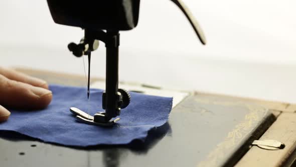 Man Sews Blue Fabric On A Vintage Sewing Machine On A Light Background