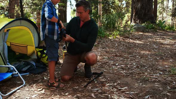 Father teaching son to use trekking pole outside tent alt