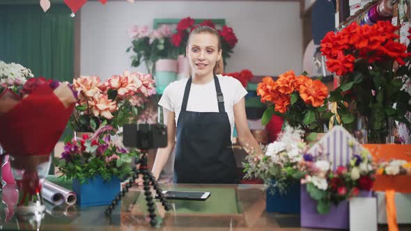 Female Florist Discusses the Order By Talking on Video Call Using a Smartphone in a Flower Shop alt