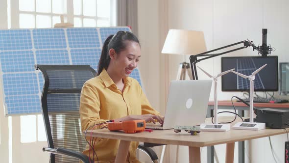 Asian Woman Sitting In Front Of Solar Cell Typing On A Laptop At The Office alt