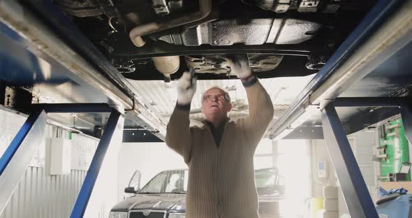 Smiling Mature Mechanic Man In A Car Service. Portrait Under The Car alt