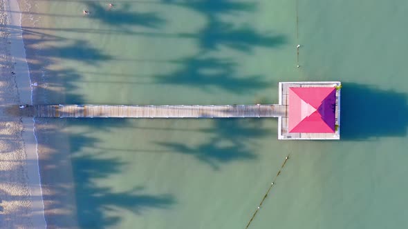 Jetty with gazebo in ocean, exotic beachfront with palms; overhead aerial riser alt