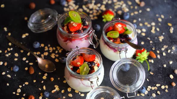Yogurt Oat Muesli and Fresh Berries in Jars Rotate on a Dark Background alt