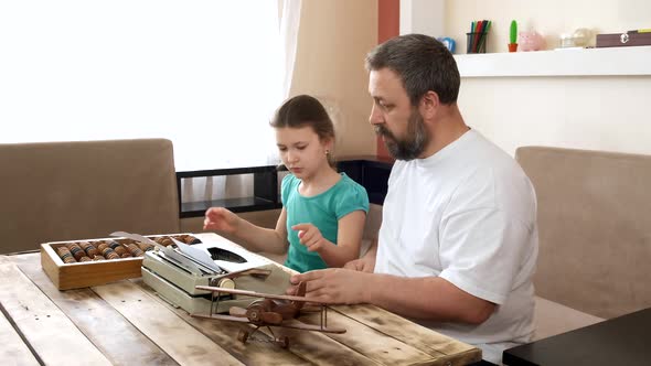 A bearded father teaches his daughter to type on an old typewriter.