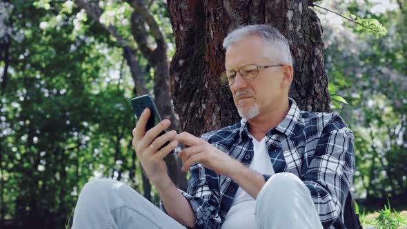 An Elderly Whitehaired Man with Glasses Talks on the Phone and Enjoys the Fresh Air and Nature