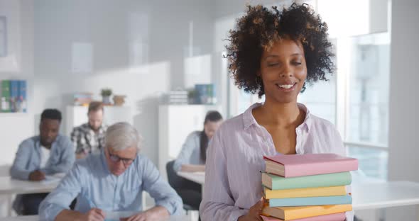 Portrait of African Teacher Holding Text Books and Smiling at Camera in Classroom alt