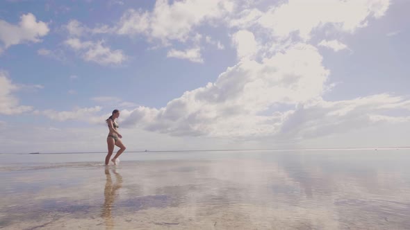 Cheerful Woman in Beach Bikini Walking on Sea Water at Shore on Blue Sky Landscape. Attractive Woman alt
