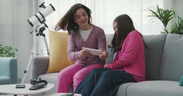 Cheerful young girls sitting on the sofa at home and connecting with a digital tablet