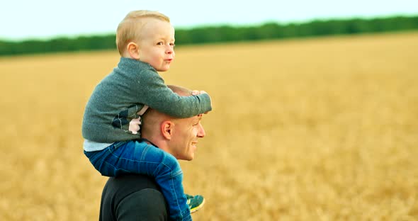 Happy Child Sits on Dad's Shoulders and Plays. Young Father Carefully Carries His Son on His alt