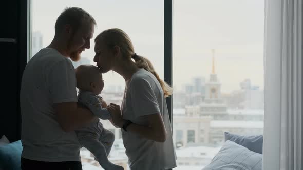 family with toddler kiss each other standing by the window overlooking the city