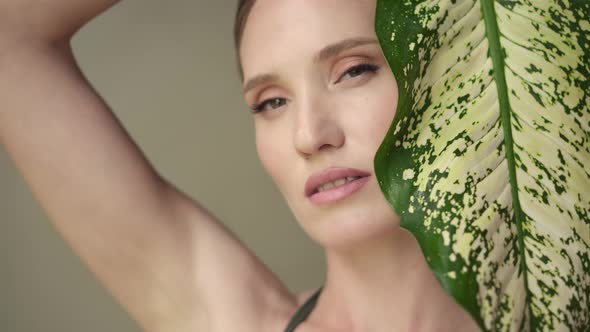 Beautiful young woman with soft and clean skin posing with tropical leaves.