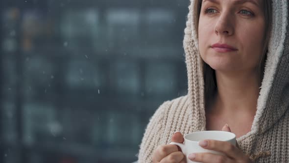 Woman Stays on Balcony During Snowfall with Cup of Hot Coffee or Tea alt
